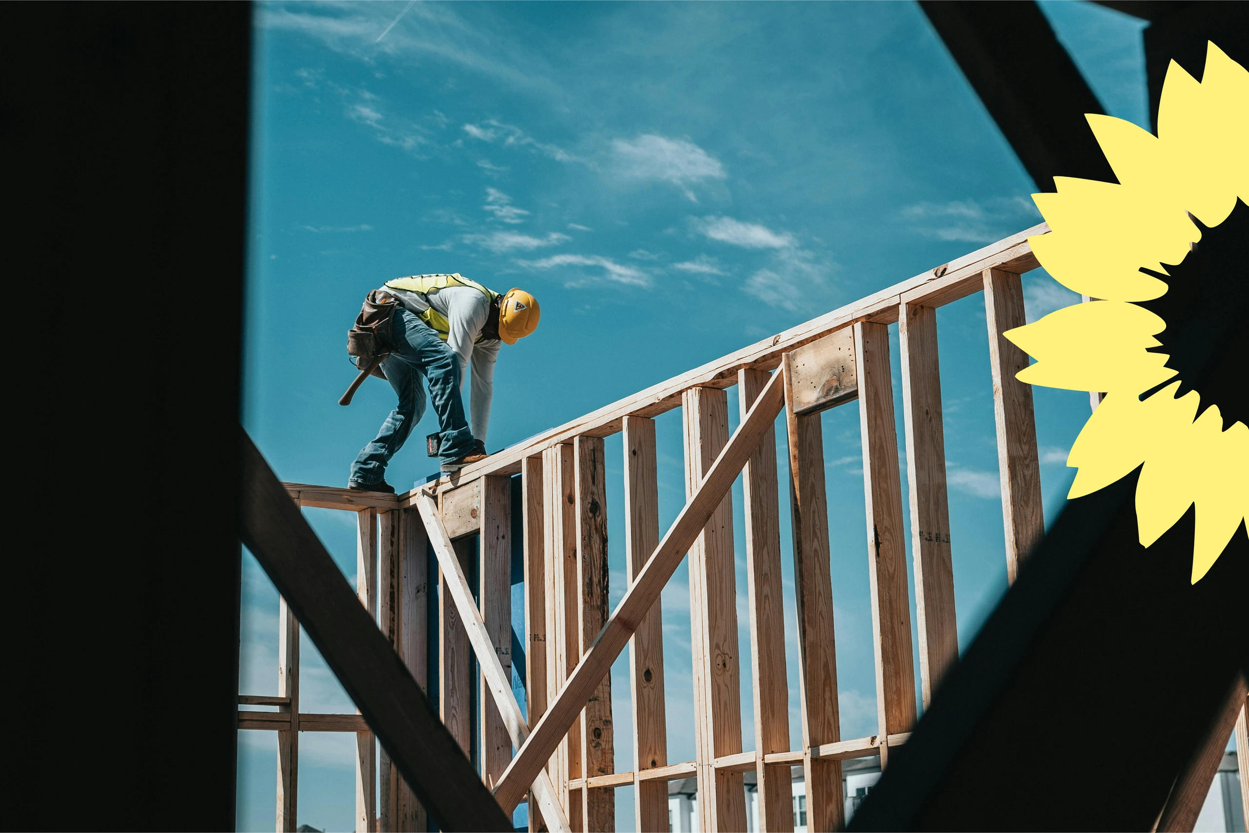 Ein Bauarbeiter mit gelbem Helm und Werkzeuggürtel arbeitet auf einem Holzrahmenbau vor blauem Himmel, daneben das Sonnenblumen-Logo der Grünen.