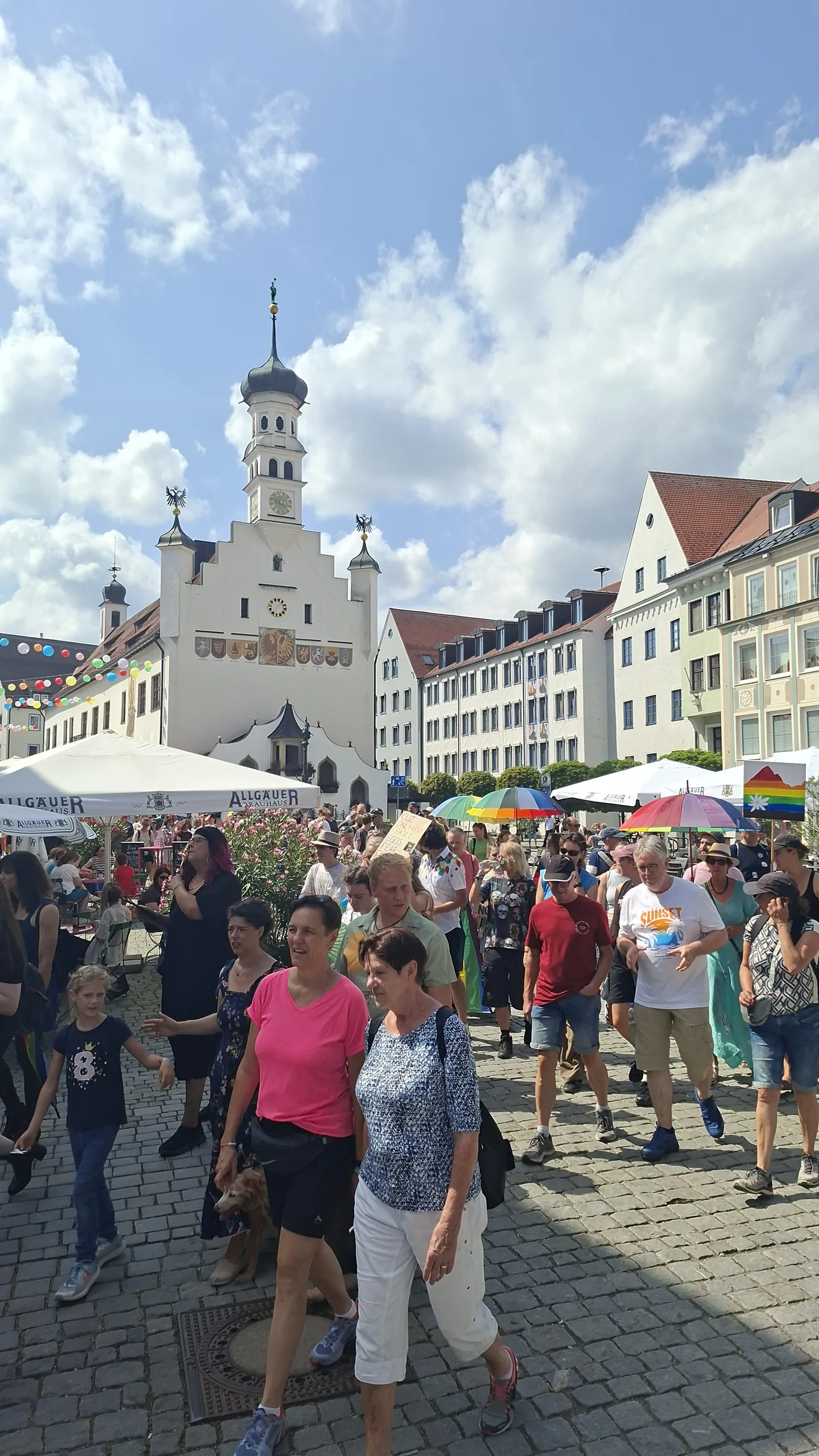 Das historische Kemptener Rathaus mit Zwiebelturm und Wappenfries, davor bunte Wimpelketten, Sonnenschirme und die Menschenmenge auf dem Platz.
