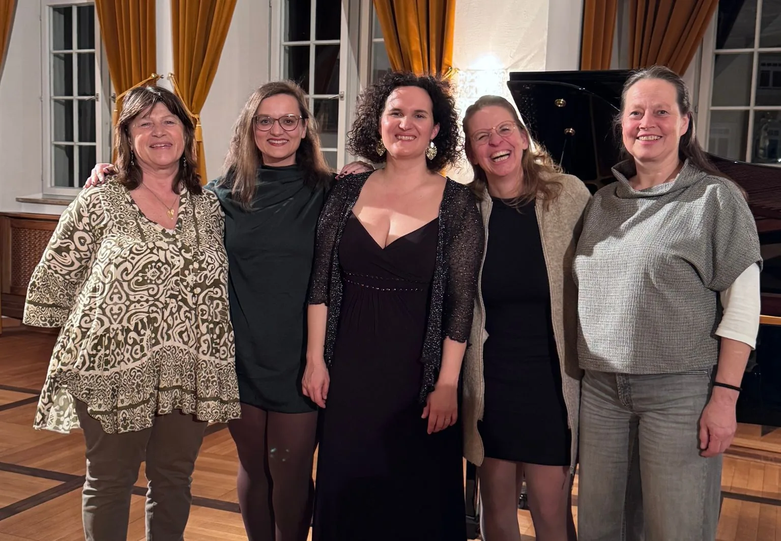 Fünf Frauen stehen lachend vor einem Flügel im Saal des Immenstädter Schlosses, in der Mitte die Pianistin im dunklen Abendkleid.